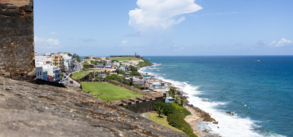 Scenic view of Old San Juan coastline in Puerto Rico, showing historic city walls, colorful buildings, and turquoise ocean waves on a sunny day