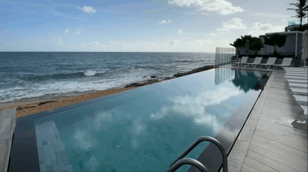 Infinity pool overlooking the ocean at Condado Ocean Club in Puerto Rico, with lounge chairs lined along the deck under a bright sky.