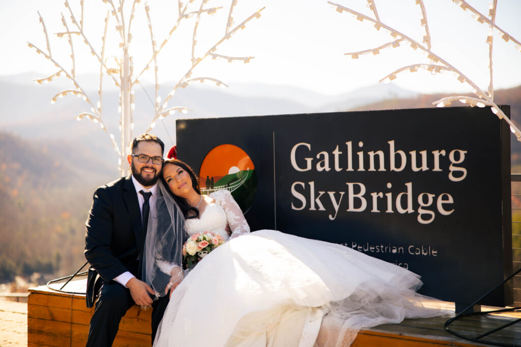 Bride and groom during their full-day elopement sitting by the Gatlinburg SkyBridge sign with mountain views in the background.